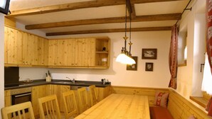 A wooden dining table with chairs, a bench, and a hanging light fixture in a room with wooden beams and a kitchen area. - Ski Lodge in Krimml With Swimming Pool (Krimml)