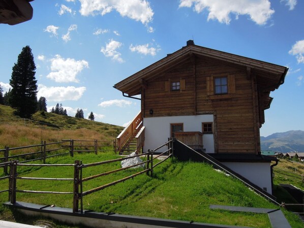 A wooden chalet with a sloped roof, a staircase leading to the entrance, and a view of the surrounding hills. - Ski Lodge in Krimml With Swimming Pool (Krimml)