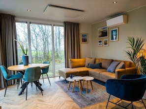 Ein modernes Wohnzimmer mit einer Couch, Sesseln, einem Esstisch und einem großen Fenster mit Vorhängen.