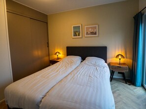 Un letto matrimoniale con due comodini, ognuno con una lampada, in una stanza con un armadio e due quadri appesi al muro.