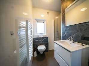 Un bagno moderno con un lavandino bianco, piastrelle di marmo scuro, un water e una finestra.