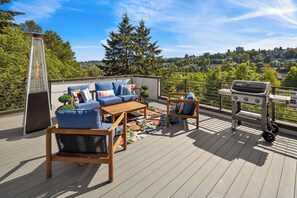 Terraza en la azotea con mobiliario exterior, una parrilla y vistas a un paisaje urbano.
