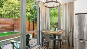 A kitchen with a wooden table, metal chairs, a stainless steel refrigerator, and a view of a garden through large windows. - Luxury Retreat with Rooftop Views, Prime Location, Grill, Outdoor Games, TV (Seattle)