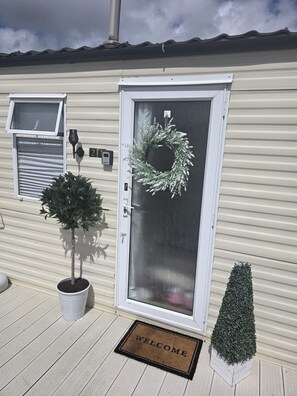 A house with a white door, a welcome mat, a potted plant, and a wreath. - Waterside Retreat T21 (Ingoldmells)