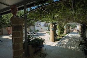 A covered outdoor area with stone pillars, potted plants, and a pathway leading to a building.