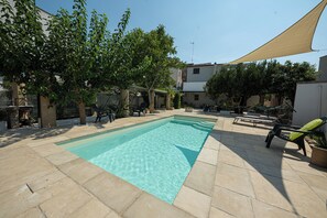 Ein rechteckiger Pool mit klarem Wasser, umrandet von Steinfliesen und beschattet durch eine große Markise.