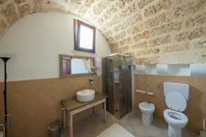 Ein Badezimmer mit einer Steinwand, einem hölzernen Waschtisch, einer Duschkabine aus Glas, einem Bidet und einer Toilette.