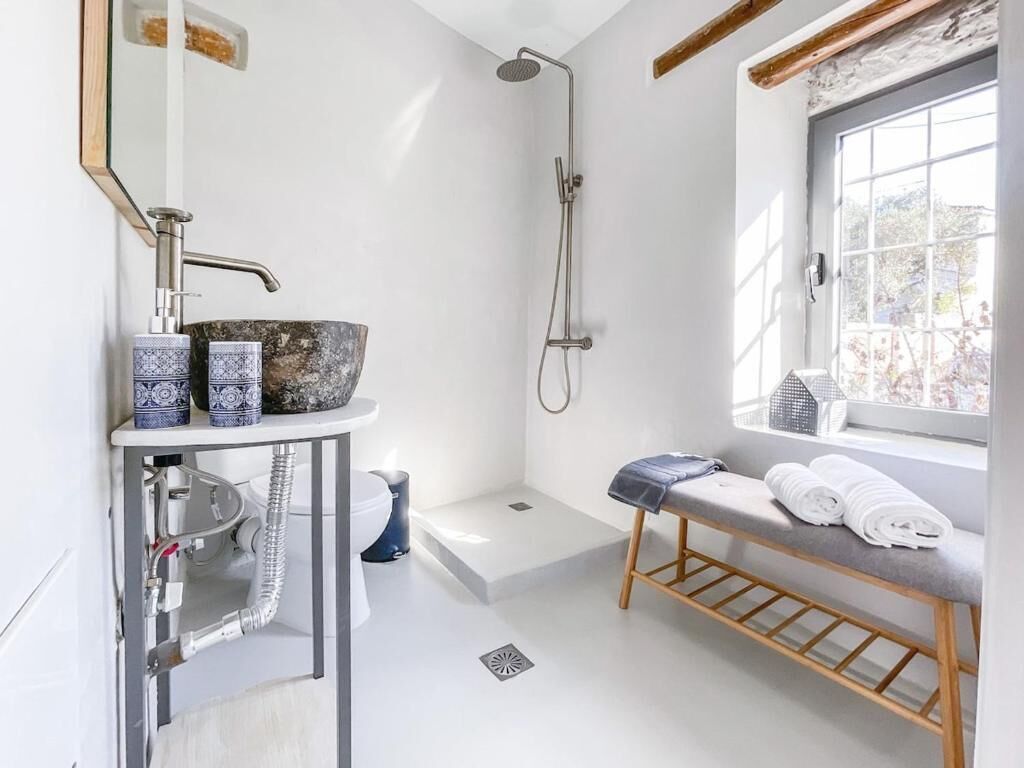 Une salle de bain moderne avec une douche, un lavabo surmonté d’un plan vasque, un banc avec des serviettes et une fenêtre offrant une vue agréable.