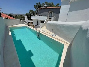 Ein Swimmingpool mit klarem, blauem Wasser, einer weißen Außenwand und einer Treppe, die zu einem Gebäude mit rotem Dach führt.