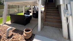 Una casa de dos pisos con un porche cubierto, una escalera y muebles de exterior.