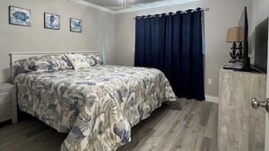 Une chambre à coucher comprenant un lit, un ventilateur de plafond, une table de chevet, une commode et un téléviseur.