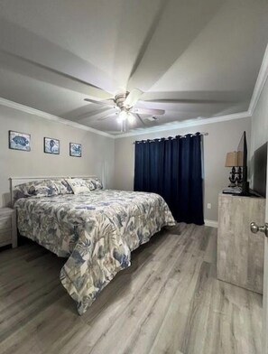 A bedroom with a bed, a ceiling fan, a nightstand, a dresser, and a TV. - Coastal Gem with River Views (Matagorda)