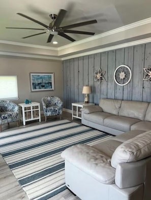 A living room with a ceiling fan, a sofa, two armchairs, a striped rug, and decorative wall art. - Coastal Gem with River Views (Matagorda)