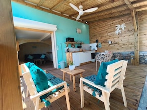 Une terrasse en bois avec deux chaises et une table, un coin cuisine équipé d’un four à micro-ondes et d’ustensiles, et un ventilateur de plafond.