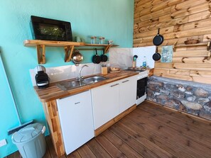 Eine kleine Küche mit Holzausziehtisch, weißen Schränken, einem eingebauten Ofen und einem Kamin aus Naturstein.