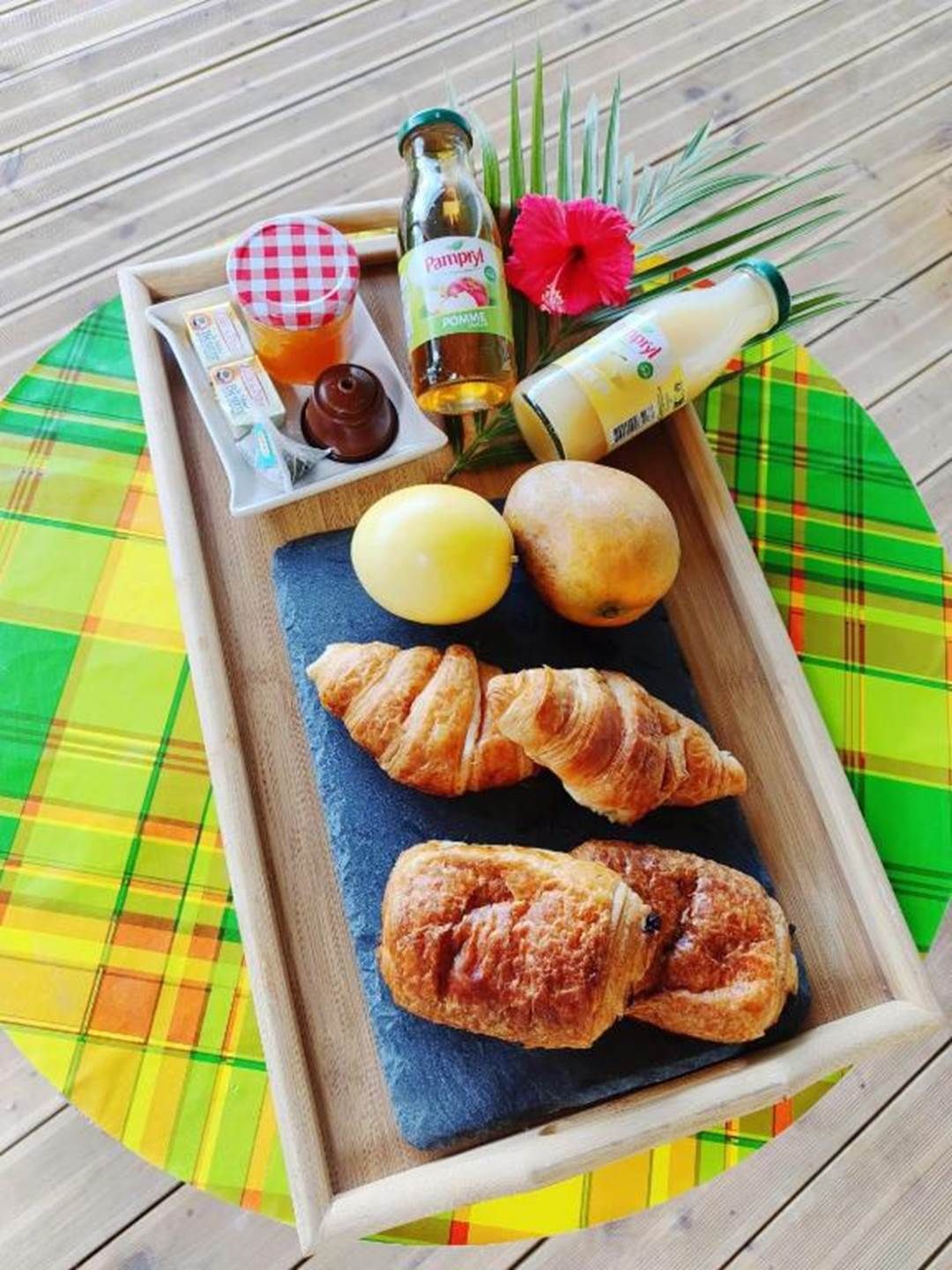 Un plateau avec des croissants, une bouteille de Pampry, une bouteille d’huile d’olive et une fleur d’hibiscus rouge.