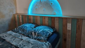 A bedroom with a wooden headboard, a bed with floral-patterned bedding, and a wall-mounted illuminated moon decoration. - Caribbean Beach Studios. Ti Colibri Studio near the beaches in Ferry-Deshaies (Deshaies)