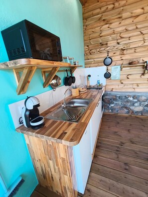 Une cuisine avec un plan de travail en bois, un évier, un four à micro-ondes et des casseroles suspendues.
