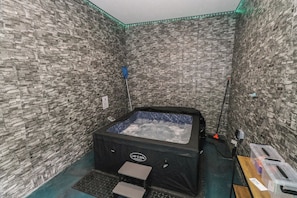 Ein Spa-Raum mit einer Wand aus Steinoptik, einer Whirlwanne und einem kleinen Tisch mit Bedienfeld.