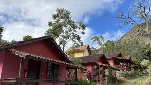 Une rangée de maisons traditionnelles aux toits rouges, avec des escaliers en pierre menant à l’entrée, entourées d’une végétation luxuriante et sous un ciel dégagé.