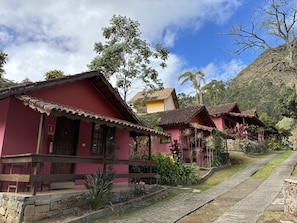 A row of traditional red-roofed houses with stone steps leading up to the entrance, surrounded by lush greenery and a clear sky.