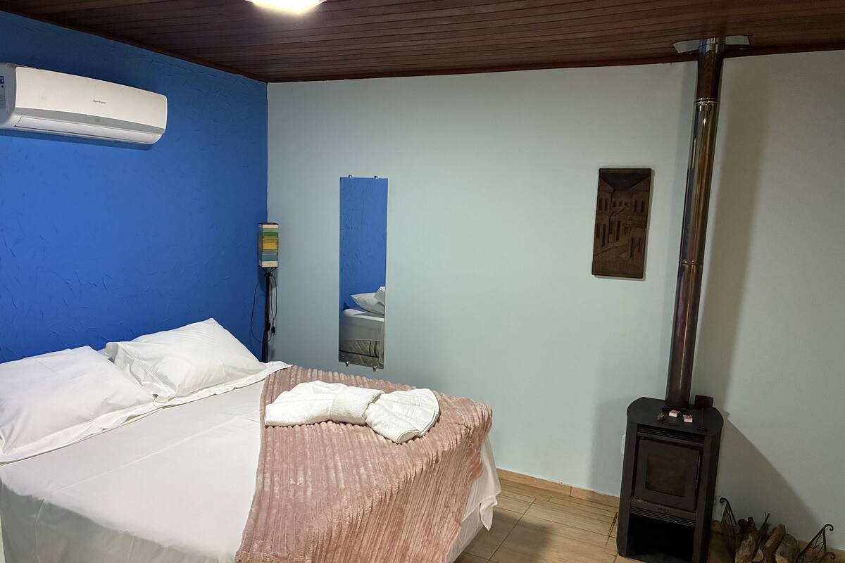 Un dormitorio con cama, espejo, calentador en la pared y estufa de leña.