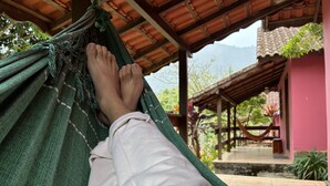 Un hamac dans lequel reposent les jambes d’une personne, un bâtiment rose et une structure en bois en arrière-plan.