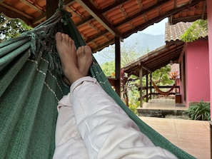 A hammock with a person's legs resting in it, a pink building, and a wooden structure in the background.