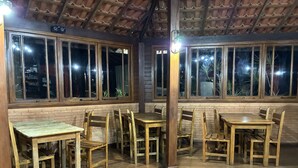 Un restaurant avec des tables et des chaises en bois, de grandes fenêtres et un mur en briques.