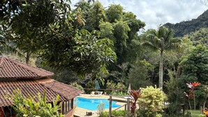 Un espace piscine doté d’un toit en carrelage, entouré d’une végétation luxuriante et avec une chaîne de montagnes en toile de fond.