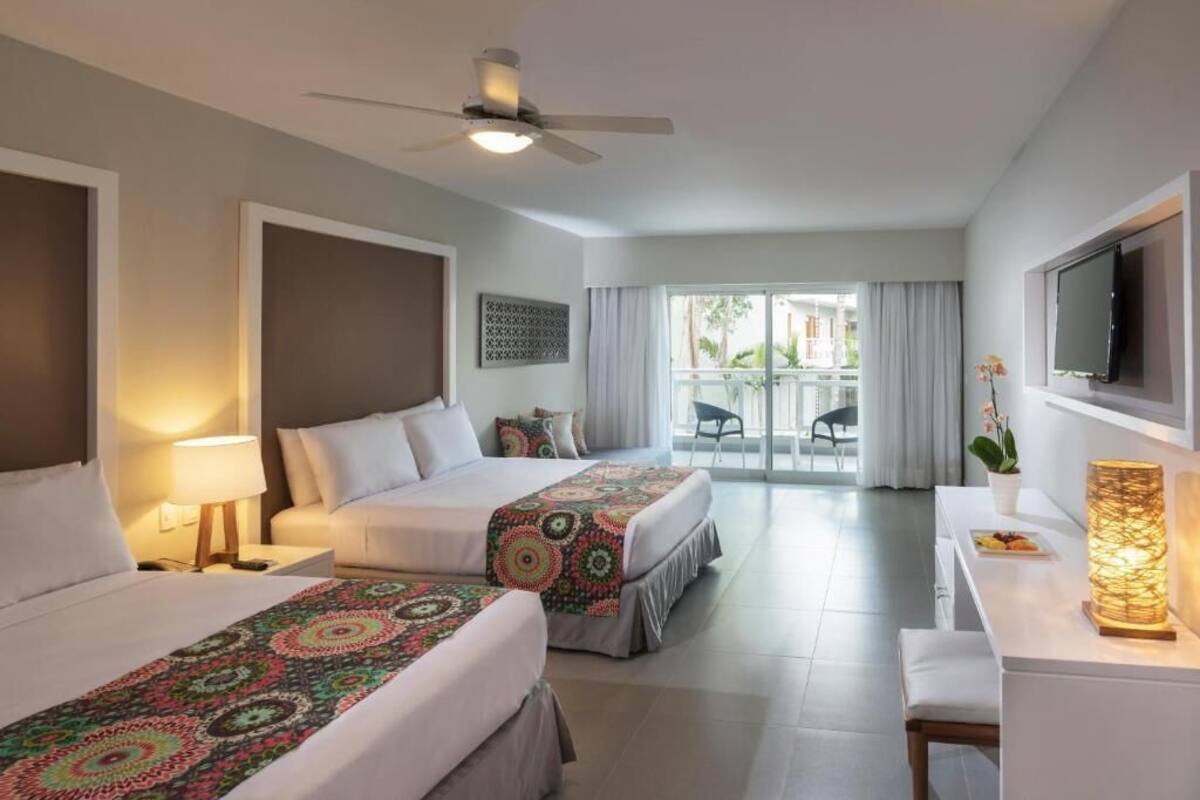 Habitación de hotel con dos camas, un escritorio, un televisor y un balcón con vistas.