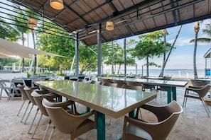 An outdoor dining area with tables and chairs, a thatched roof, and a view of the ocean. - Emotions by Hodelpa - Juan Dolio (Juan Dolio)