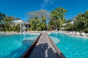 Ein Pool mit Holzterrasse, umgeben von Liegestühlen und Palmen.