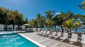 A poolside area with lounge chairs, a wooden deck, and a view of the ocean. - Emotions by Hodelpa - Juan Dolio (Juan Dolio)
