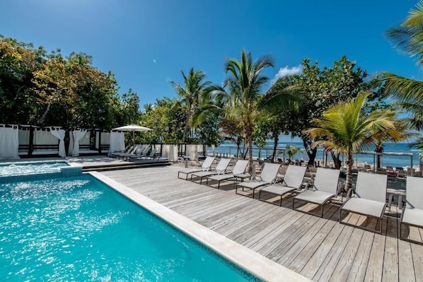 A poolside area with lounge chairs, a wooden deck, and a view of the ocean. - Emotions by Hodelpa - Juan Dolio (Juan Dolio)