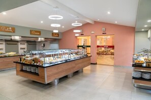 A buffet area with multiple food stations, a clear exit sign, and a seating area in the background.