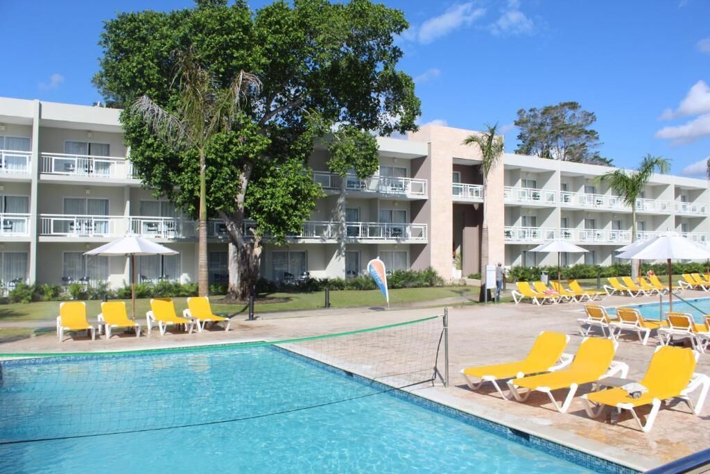 A hotel with a swimming pool, yellow lounge chairs, and a multi-story building with balconies.