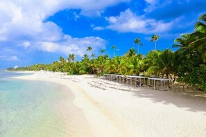 A beach with clear turquoise water, white sand, and palm trees.