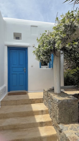 A white building with a blue door, stone steps, and a small window.. Theros Poros