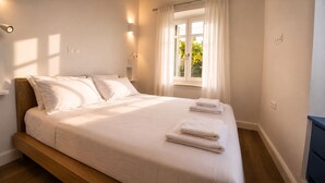 Una cama bien tendida con almohadas y toallas dobladas, una ventana con cortinas y luces fijadas en la pared.