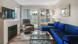 Una sala de estar con chimenea, un sofá azul, una mesa de centro de vidrio y un televisor sobre un mueble.
