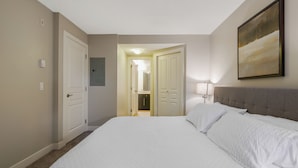 Habitación de hotel con una cama grande, cabecera, un cuadro en la pared y una puerta que da a un baño.
