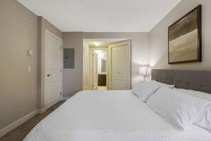 Habitación de hotel con una cama grande, cabecera, un cuadro en la pared y una puerta que da a un baño.