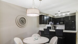 Una cocina moderna con armarios oscuros, una isla de mármol y una zona de comedor con sillas blancas.