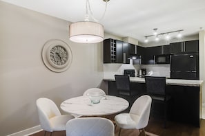 Una cocina moderna con armarios oscuros, una isla de mármol y una zona de comedor con sillas blancas.