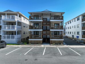 Ein mehrstöckiges Wohnhaus mit Balkonen und einem Parkplatz davor, bewölkter Himmel.