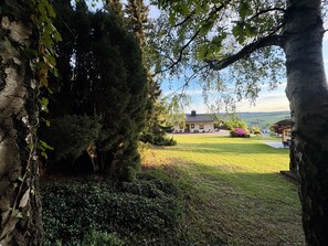 A house with a grassy yard, a tree, and a view of the countryside.