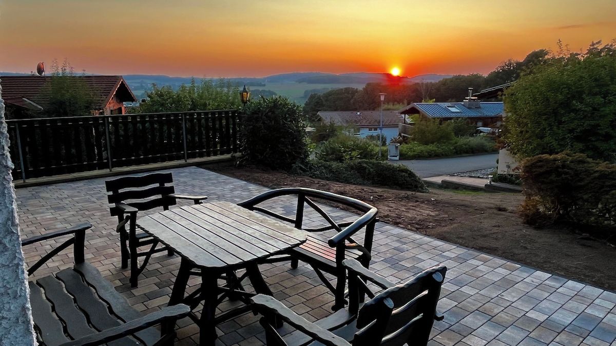 Eine Terrasse mit Tisch und Stühlen, mit Blick auf eine Wohngegend bei Sonnenuntergang.