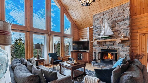 A spacious living room with large windows, a stone fireplace, and comfortable seating. - Spa, Pool & Sauna | Sérénité des Laurentides (Mille-Isles)