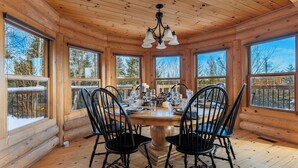 A wooden cabin interior with a dining table set for four, surrounded by large windows. - Spa, Pool & Sauna | Sérénité des Laurentides (Mille-Isles)